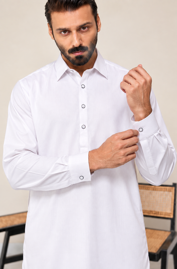 A man wearing a white long-sleeve button-up shirt with a collar and cuff buttons, shown from the waist up against a light beige indoor background.